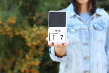 Woman in denim jacket holds white block wooden calendar with date April 17 outdoors
