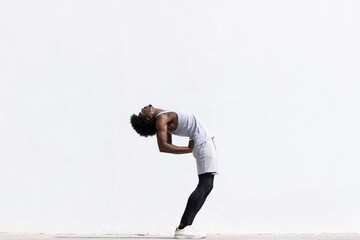 Black athlete stretching body over white wall