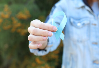 Woman in denim jacket holding blue awareness ribbon outdoors