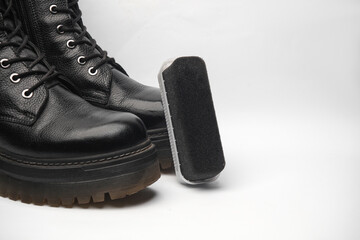 Leather boots and a sponge with shoe polish on a white background