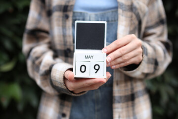 Woman holds calendar with the date May 9 outdoors.