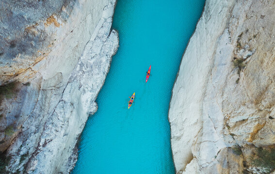 High angle view of unrecognizable people kayaking on blue narrow river flowing between rocky mountains during vacation at daytime