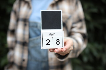 Woman holds calendar with the date May 28 outdoors.
