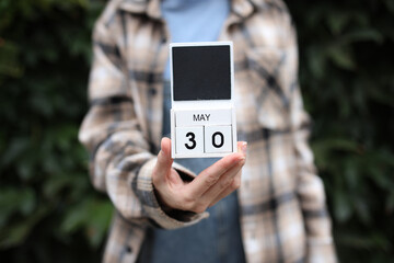 Woman holds calendar with the date May 30 outdoors.