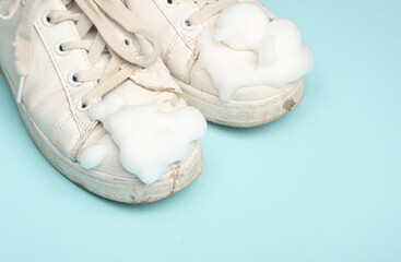 Old White sneakers with cleaning foam  on a blue background. Shoe care