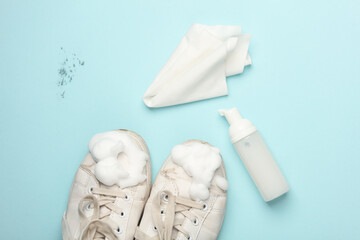 White sneakers with cleaning foam and a rag on a blue background. Shoe care