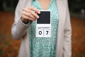 Woman holds calendar with the date september 7 outdoors.