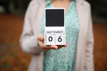 Woman holds calendar with the date september 6 outdoors.