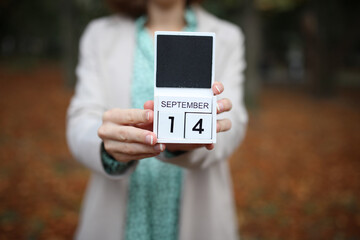 Woman holds calendar with the date september 14 outdoors.
