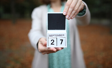 Woman holds calendar with the date september 27 outdoors.