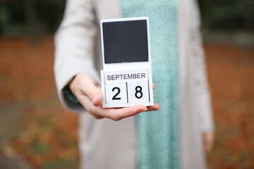 Woman holds calendar with the date september 28 outdoors.