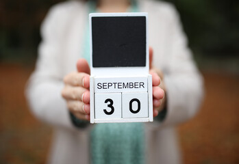 Woman holds calendar with the date september 30 outdoors.