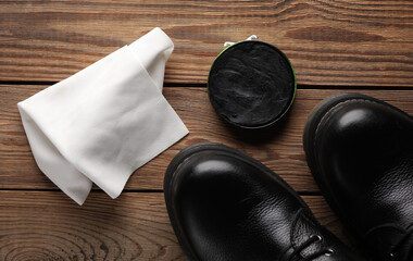 Black leather boots with shoe polish and rag on wooden background. Shoes care
