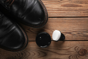 Black leather boots with shoe polish and sponge on wooden background. Shoes care