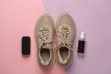 Sneakers with sponge and spray bottle on pink background. Shoe care. Top view. Flat lay