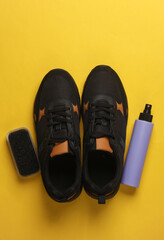 Sneakrers with brush and spray bottle on yellow background. Shoe care