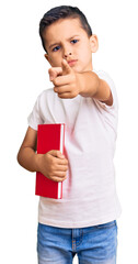 Little cute boy kid reading a book pointing with finger to the camera and to you, confident gesture looking serious