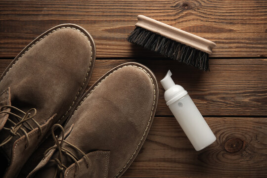 Suede shoes with cleaning foam and brush on wooden background. Shoe care
