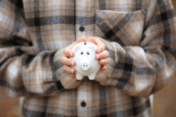 Woman in warm shirt holds piggy bank outdoors in autumn park