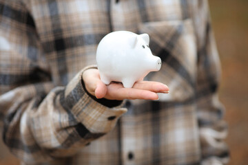 Woman in warm shirt holds piggy bank outdoors in autumn park
