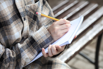 Woman in a warm shirt with sketchbook and pencil on a bench in an autumn park