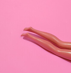Summer minimal concept. Legs of doll are sunbathing on pink background