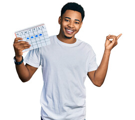 Young african american man holding rainy weather calendar smiling happy pointing with hand and finger to the side
