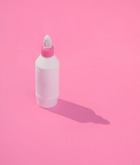 Bottle of glue on pink background with a long shadow. Minimalist photo
