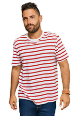 Obraz premium Handsome man with beard wearing striped tshirt with serious expression on face. simple and natural looking at the camera.