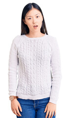 Young beautiful chinese woman wearing casual sweater in shock face, looking skeptical and sarcastic, surprised with open mouth