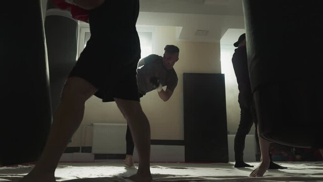 Fighters team exercise with punching inventory in sports club. Kick-boxers do kicks and punches in fighting gym slow motion. Combat techniques