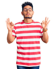 Naklejka premium Handsome latin american young man wearing casual clothes and glasses relaxed and smiling with eyes closed doing meditation gesture with fingers. yoga concept.