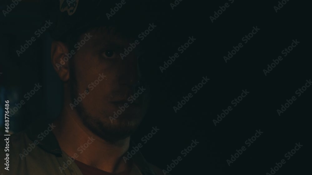 Poster portrait of a tired worker in a helmet and uniform in the process of working on a metal product. fac