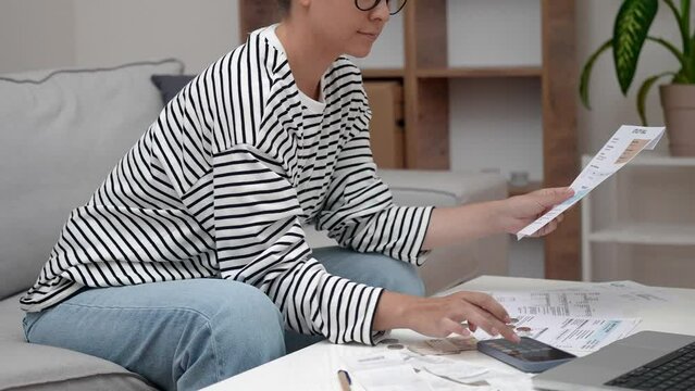Lady calculates expenses involved in financial paperwork focused woman in striped sweater holds documents with monthly banking payments summarizing utility bills at home