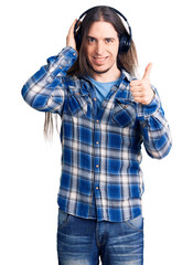 Obraz na płótnie Canvas Young adult man with long hair listening to music using headphones smiling happy and positive, thumb up doing excellent and approval sign