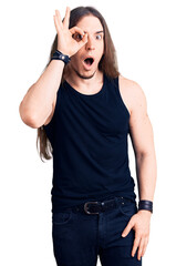 Young adult man with long hair wearing goth style with black clothes doing ok gesture shocked with...