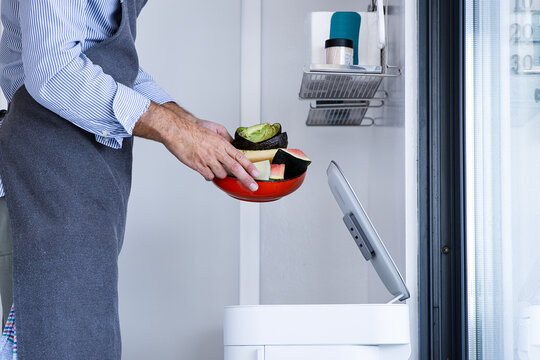 Unrecognizable man chef in apron standing with fruits waste near automatic trash bin