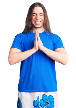 Young adult man with long hair wearing swimwear praying with hands together asking for forgiveness smiling confident.