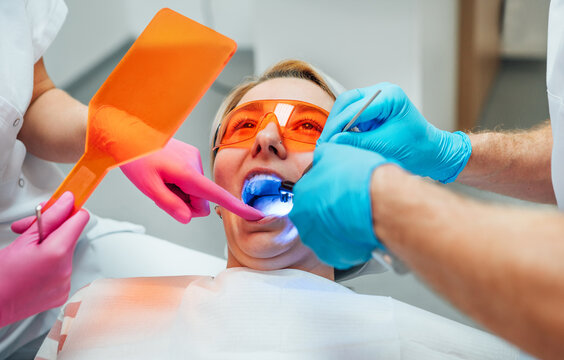 Young woman in protective eyeglasses during teeth composite filling material polymerization procedure with curing UV light at dentist's office. Health care, teeth beauty and medicare industry concept.