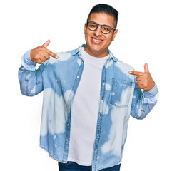 Young latin man wearing casual clothes and glasses looking confident with smile on face, pointing...