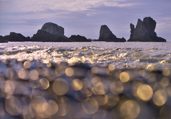 Sparkling ocean waves with rocky silhouette at dusk