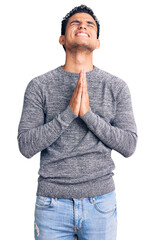 Hispanic handsome young man wearing casual sweater begging and praying with hands together with...