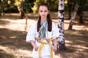 Young girl wearing karate fighter uniform and medals holding trophy. Karateka champion