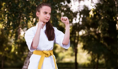 Fototapete Practice. Karate, taekwondo girl with yellow belt doing martial arts outdoor. Little female model, sport kid training in motion and action. Sport, movement, childhood concept. © VlaDee