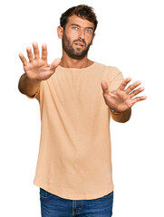 Handsome young man with beard wearing casual tshirt doing stop gesture with hands palms, angry and frustration expression