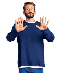 Handsome blond man with beard wearing casual sweater moving away hands palms showing refusal and denial with afraid and disgusting expression. stop and forbidden.
