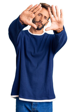 Handsome blond man with beard wearing casual sweater doing frame using hands palms and fingers, camera perspective