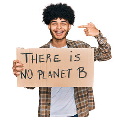 Young african american man with afro hair holding there is no planet b banner pointing finger to...