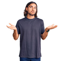 Young handsome man wearing casual clothes clueless and confused expression with arms and hands...