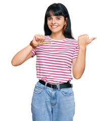 Young hispanic girl wearing casual clothes pointing to the back behind with hand and thumbs up, smiling confident